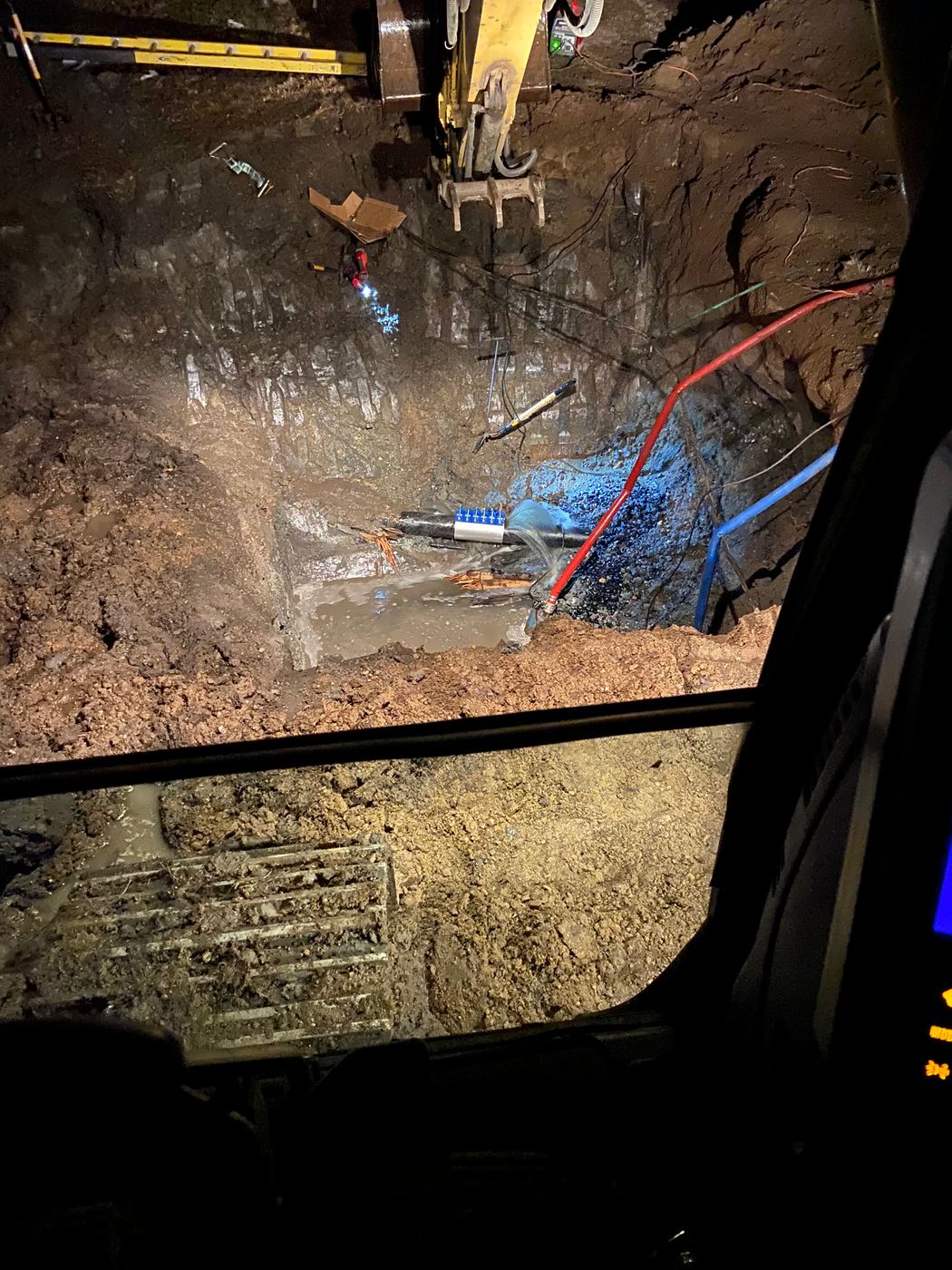Night water main repair lit from an excavator cab