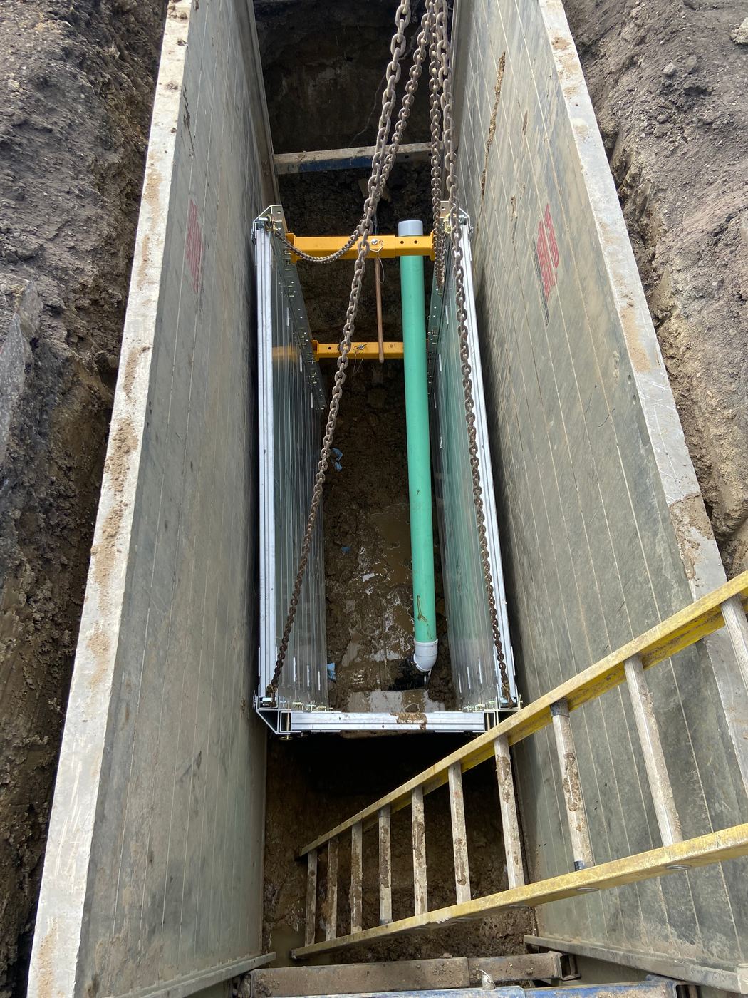 Shored trench with new sewer pipe and access ladder on a street reconstruction